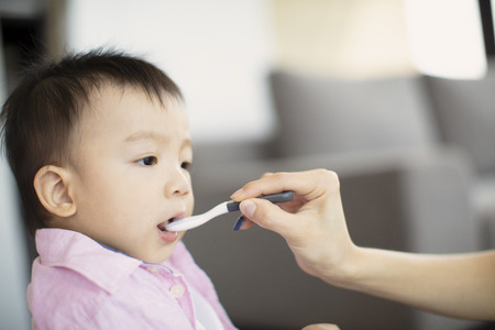 Mother feeding baby with spoon indoorsの写真素材
