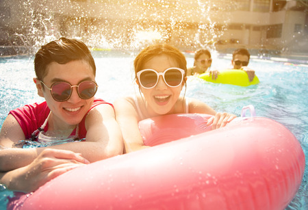 Happy friends playing in swimming pool on summer vacation