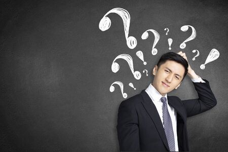 confused young businessman scratching his head with question markの写真素材
