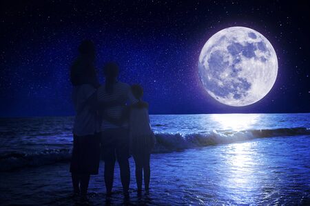 Family standing on beach and watching the moon. Celebrate Mid-autumn festival togetherの写真素材