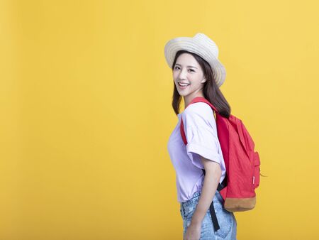 smiling woman with backpack standing on yellow background