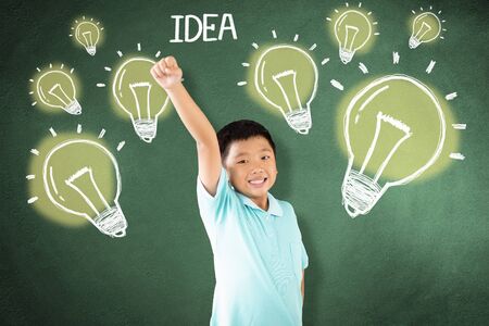 kid standing against chalkboard with idea bulb conceptの写真素材