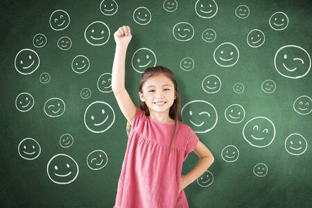 little girl standing against chalkboard and face icon on the boardの写真素材