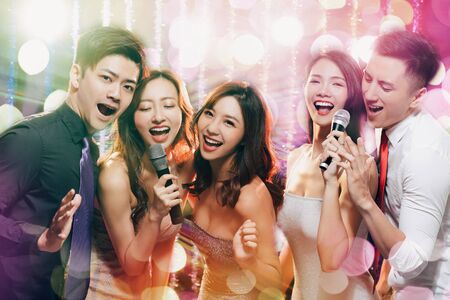young group holding microphone and singing at karaokeの写真素材