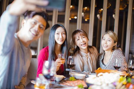 Happy friends taking selfie in hot pot restaurantの写真素材