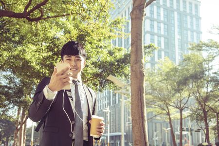 Businessman holding mobile phone while walking on street to officeの写真素材