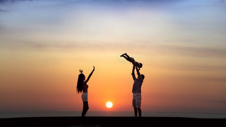 happy family playing on the beach at sunsetの写真素材