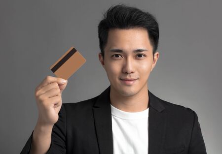 young asian business man showing credit card isolated over gray backgroundの写真素材