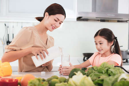 mother working at kitchen and daughter showing health foodの写真素材
