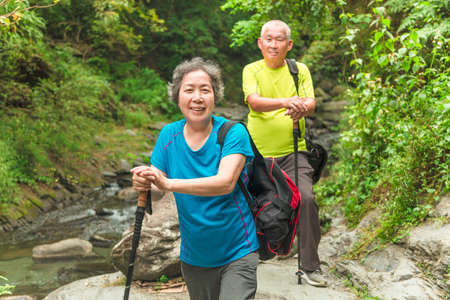 Senior couple walking across small river in nature park