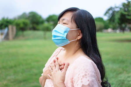 Asian woman in mask and feels unhealthy put hand where is lungs, suffering from repeated coughing and breath difficulties.の写真素材