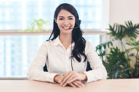 Head shot portrait confident young businesswoman looking at camera and talking by headphone.の写真素材