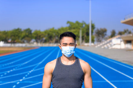Man in medical mask standing on track and ready to runの写真素材
