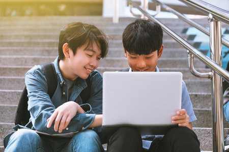Happy teenager students looking at laptop and sitting on the stairs