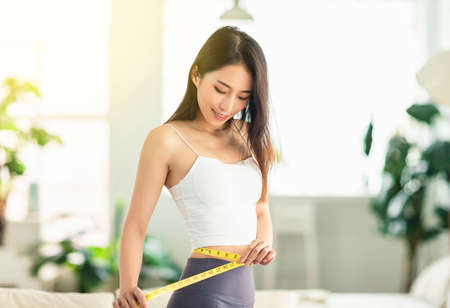 young woman confidently measured her waist circumference, satisfied with her posture, and very happy to lose weightの写真素材