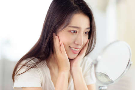 Asian young woman looking at her face in mirrorの写真素材