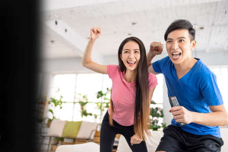 Excited Young Couple watching sports game on tv and having fun at homeの写真素材