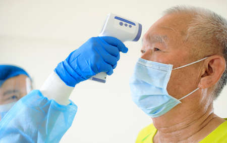 Nurse use an Infrared thermometer equipment to check the temperature on the forehead of senior man