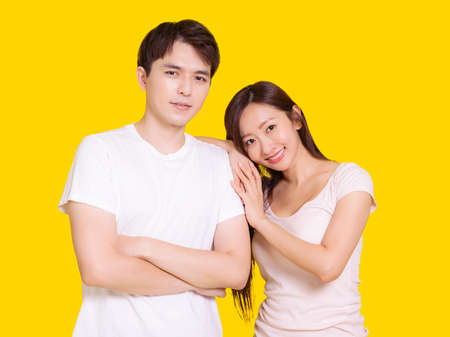 Young couple smiling at camera while woman putting her head on male shoulder .Isolated over yellow...