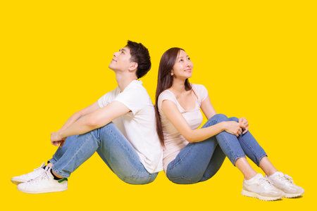 Stressed Young couple sitting back to back.Holding head.Self protection. Isolated on yellow background.の写真素材