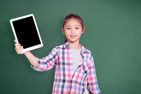 Happy student girl showing tablet. Isolated on green chalkboard background.の写真素材