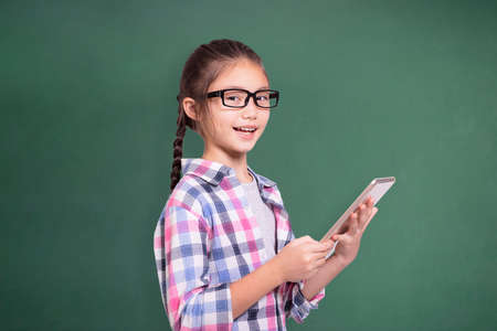 Happy student girl with glasses using tablet.Isolated on green chalkboard background.の写真素材