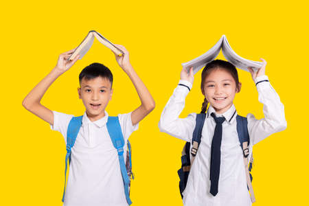 Happy student boy and girl holding book on head.Isolated on yellow background.の写真素材