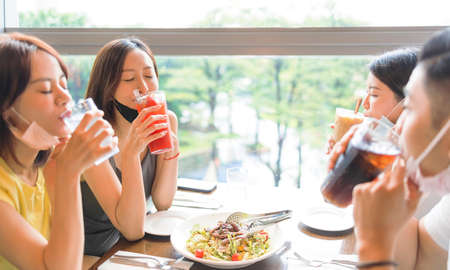 Happy Friends drinking juice in  restaurant  with face mask on to be protectedの写真素材