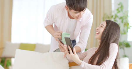 Happy young couple sitting on couch and looking at mobile phoneの写真素材