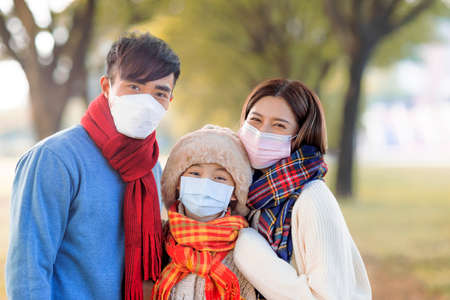 Happy family wearing medical mask and walking in the fall parkの写真素材