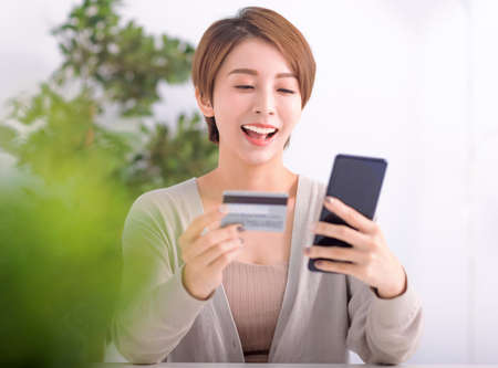 Happy young woman shopping online with mobile phone and credit card