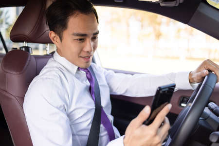 Young business man watching mobile phone in the carの写真素材