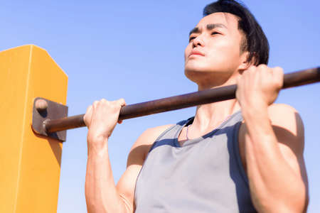 Young man exercising and holding his upper body above horizontal bar