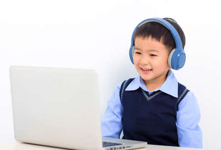 Happy little boy doing homework and learning on the laptop