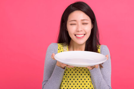 Happy young woman holding empty white plate and smellingの写真素材