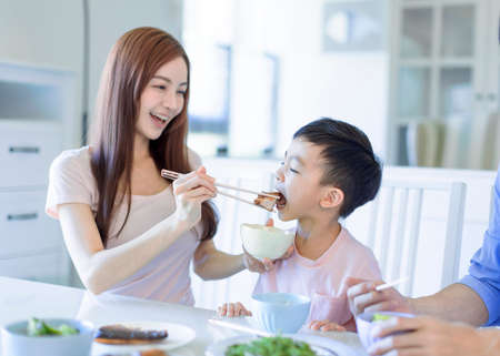 little boy enjoy eating food with father and mother. Happy Asian family having dinner at homeの写真素材