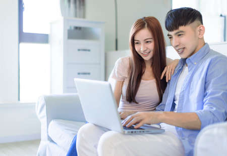 young happy happy family couple resting on sofa in living room searching internet on laptopの写真素材
