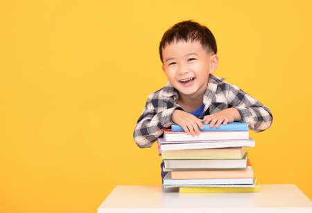 Happy little boy holding large books isolated on yellow backgroundの写真素材