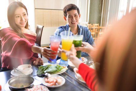 Happy Young people toasting and having dinner in hot pots restaurantの写真素材