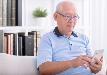 Senior man sitting on couch and browsing mobile phoneの写真素材