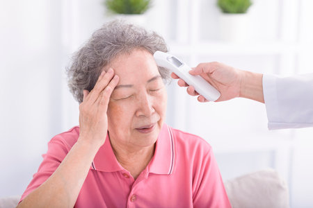 Caregiver measuring temperature to senior woman with digital thermometerの写真素材