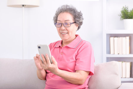 Senior woman sitting on couch and browsing mobile phoneの写真素材