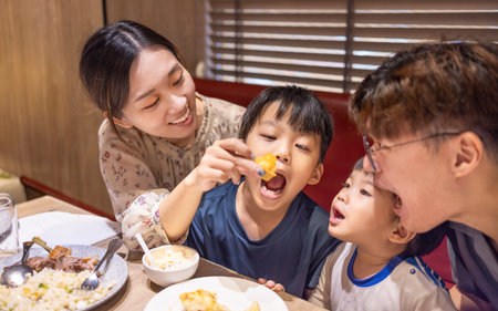 Happy mother feeds her family in restaurantの写真素材