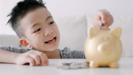 Happy asian boy putting coins into piggy bankの写真素材