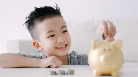 Happy asian boy putting coins into piggy bankの写真素材