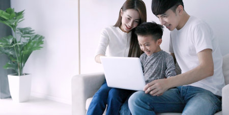 Parents with child watching funny videos using laptop browsing online tv streaming enjoying spending time together at home in living room sitting on sofaの写真素材