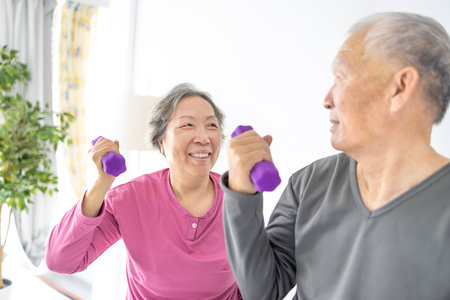 Happy Asian senior couple doing exercises with dumbbells indoors.の写真素材