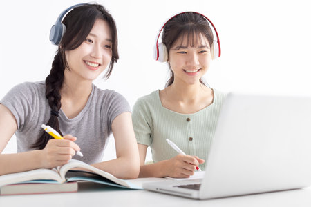 Happy young girls with wireless headphones looking at laptop screen, reading listening online courses, studying remotely from homeの写真素材
