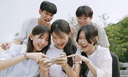 Happy young group of friends using phone and smiling together outdoor.の写真素材