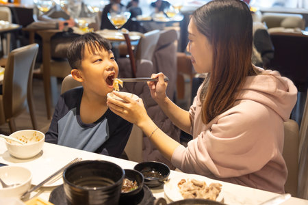 Happy Young Mother Feeding Her Son in Restaurant